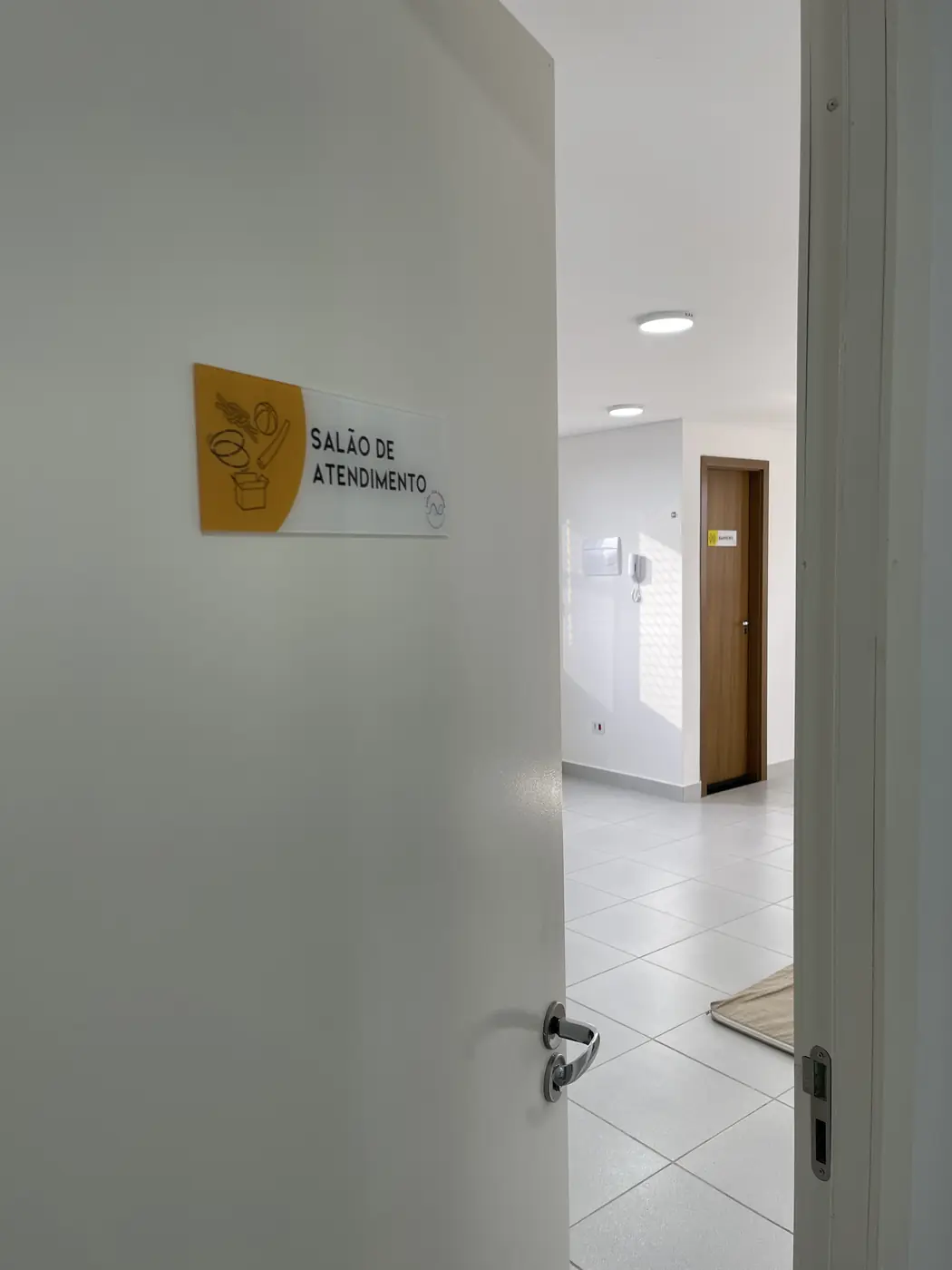 Porta aberta da clínica com a placa "Salão de Atendimento" na parede