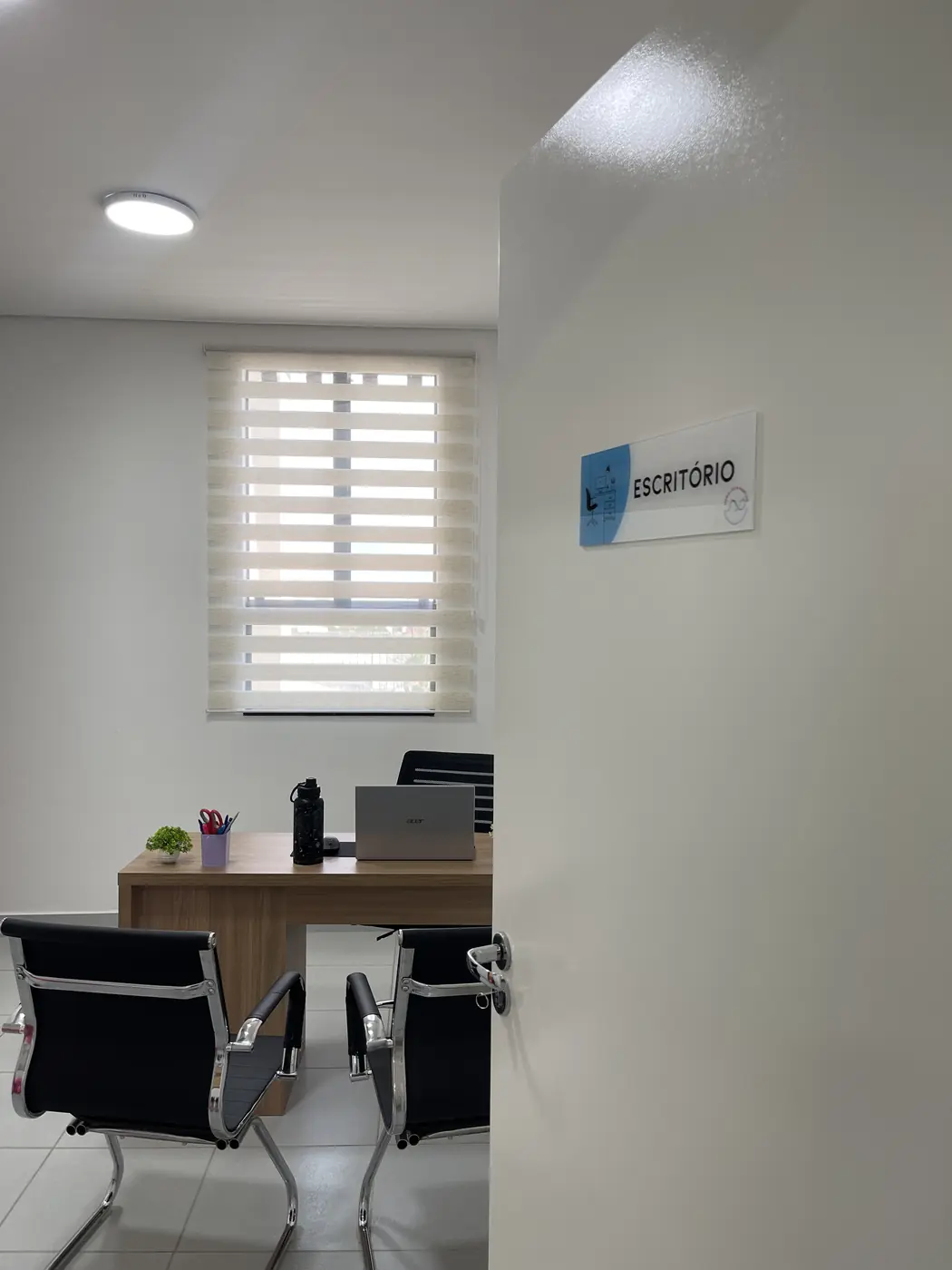 Escritório da clínica com mesa, cadeiras e a placa "Escritório" na parede