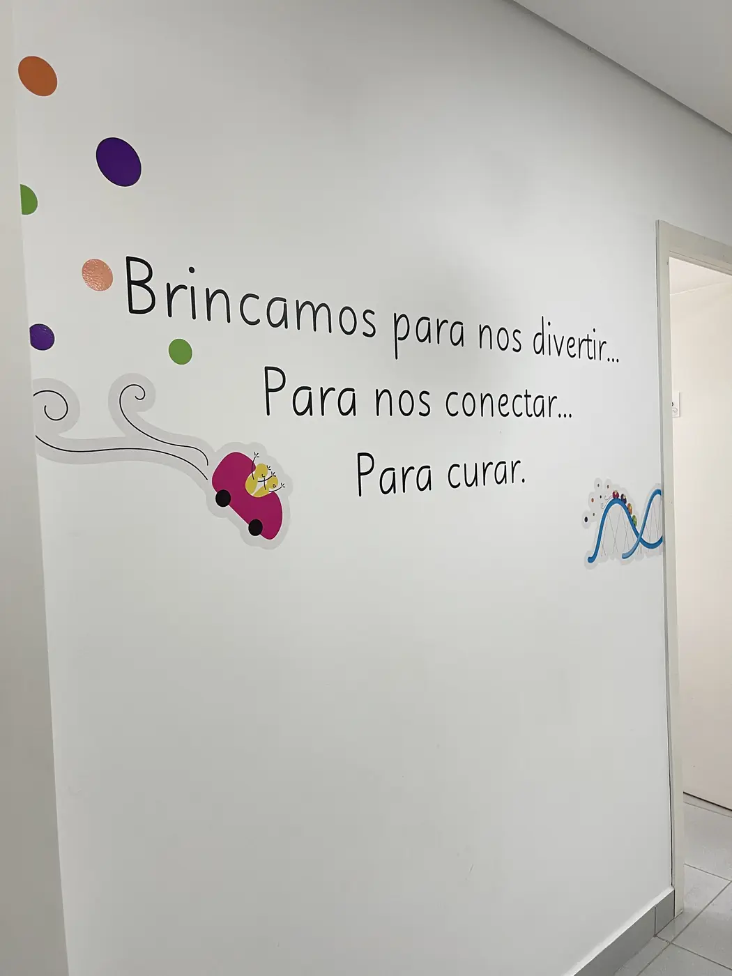 Frase pintada na parede da clínica: "Brincamos para nos divertir... Para nos conectar... Para curar."