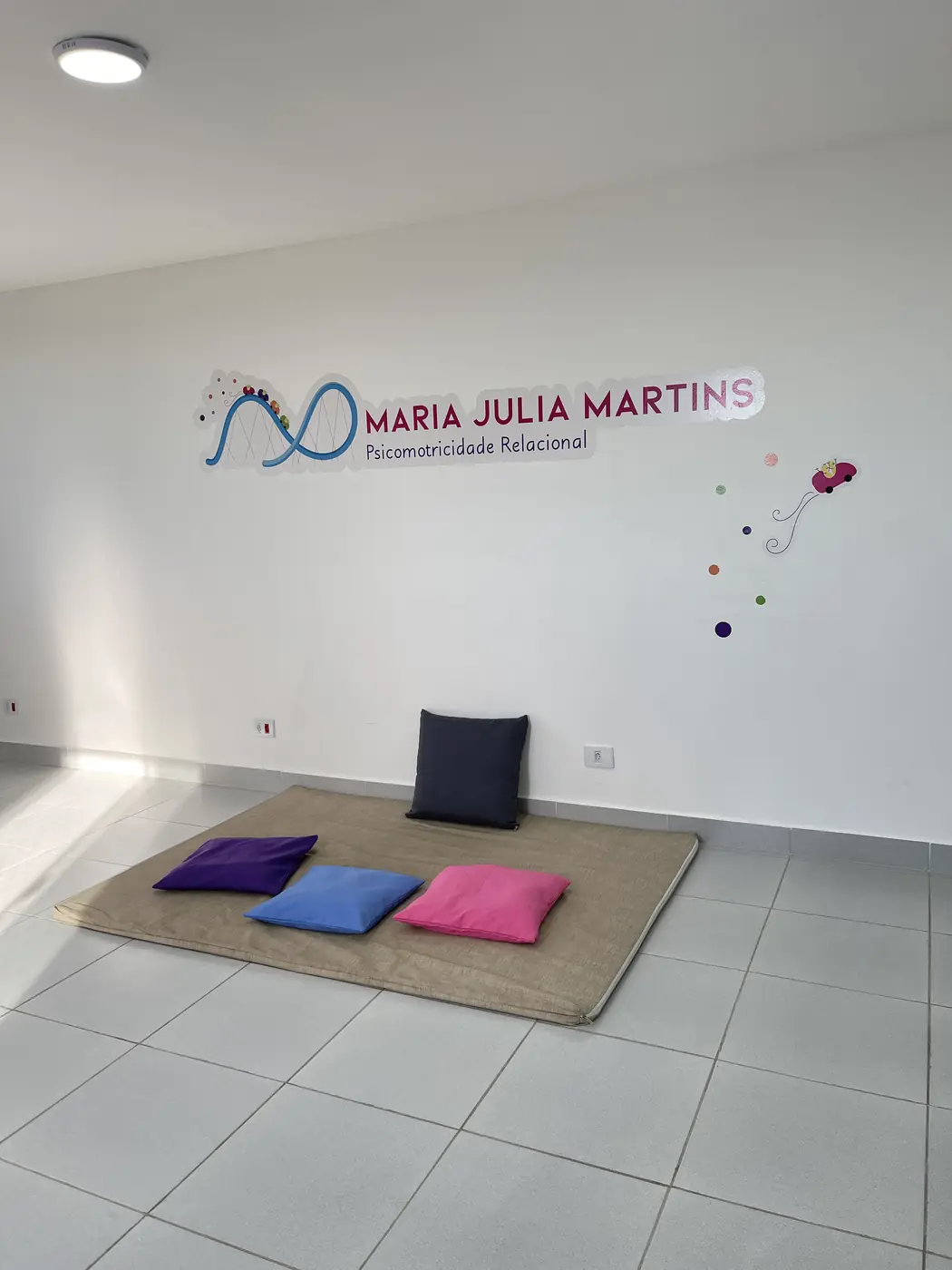 Salão de atendimento com o logotipo Maria Julia Martins na parede e almofadas coloridas sobre um tapete